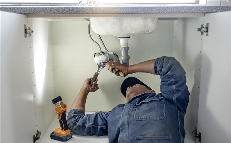Plumber repairing pipes beneath a bathroom sink in Pinellas Park