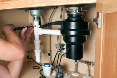 Plumber repairing a garbage disposal beneath a kitchen sink in Pinellas Park