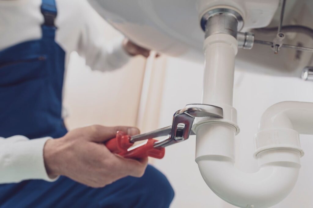 Plumber repairing a white drain pipe beneath a sink in Pinellas Park